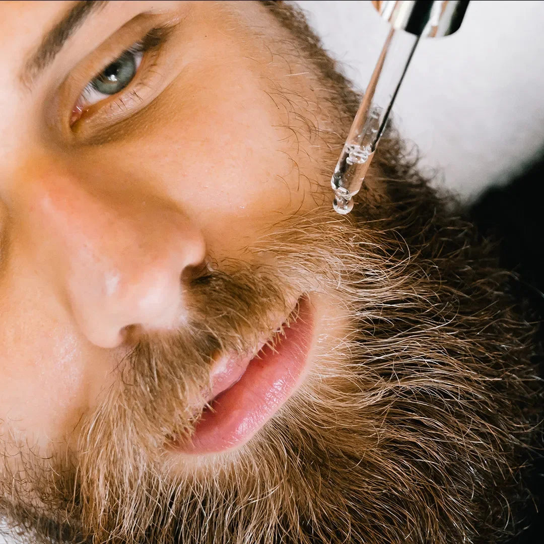 Close-up of man applying beard oil with dropper to thick beard, natural grooming product