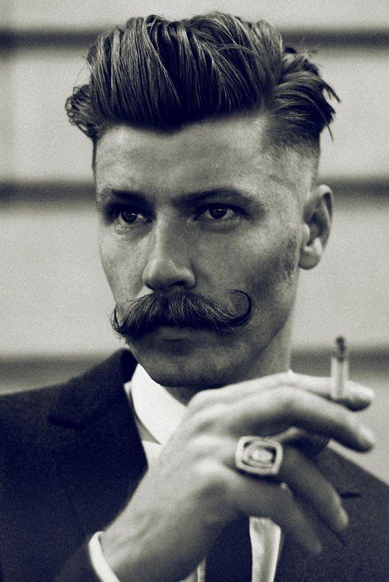 Man with styled handlebar moustache, slicked-back hair, and wearing a suit