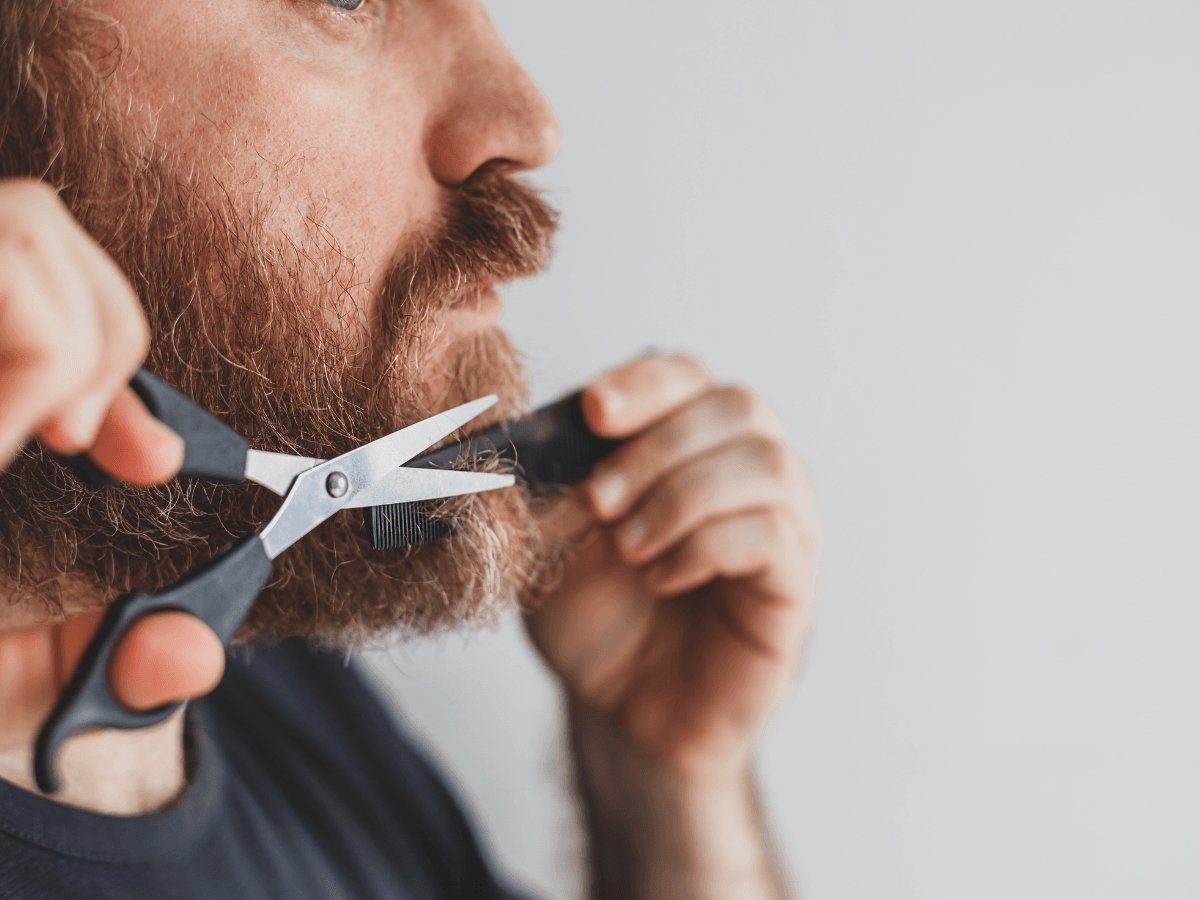 Man trimming beard with scissors and comb, close-up grooming shot