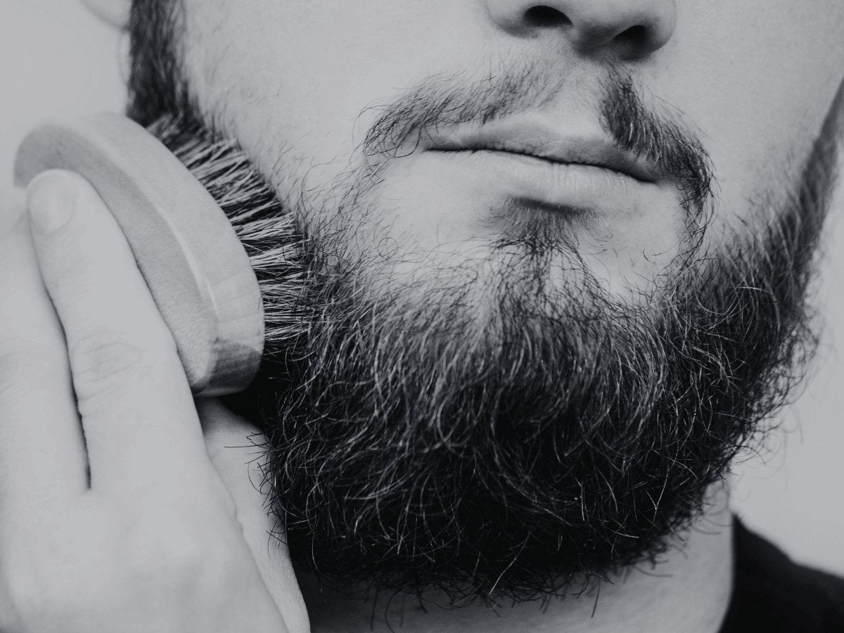 Close-up of a man brushing his beard with a wooden bristle brush for beard grooming