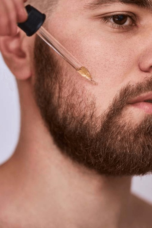 Close-up of man applying beard oil with dropper to facial hair