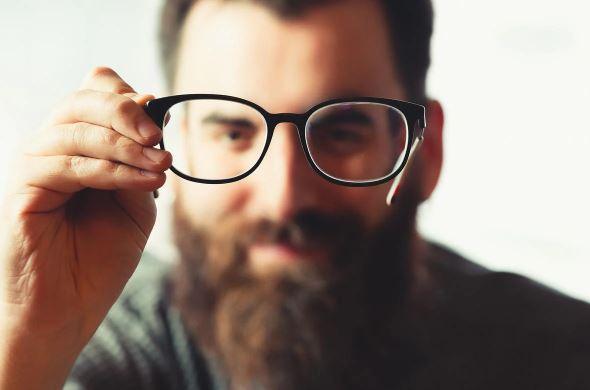 Bearded man holding eyeglasses, showcasing thick facial hair and men's grooming style