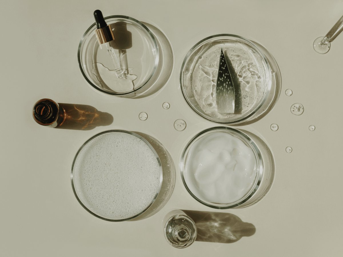 Natural beard oil ingredients in glass bowls, including gel, serum, and a dropper.