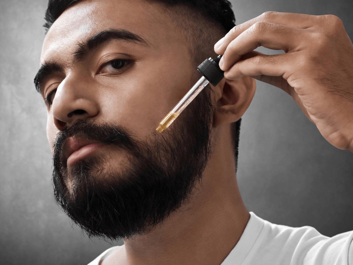 Man applying beard oil with dropper to groomed black beard
