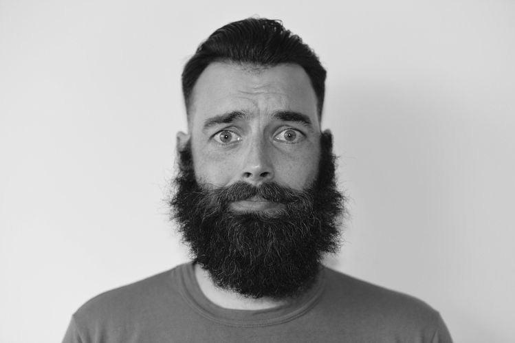 Bearded man with styled dark hair looking uncertain, promoting natural beard care
