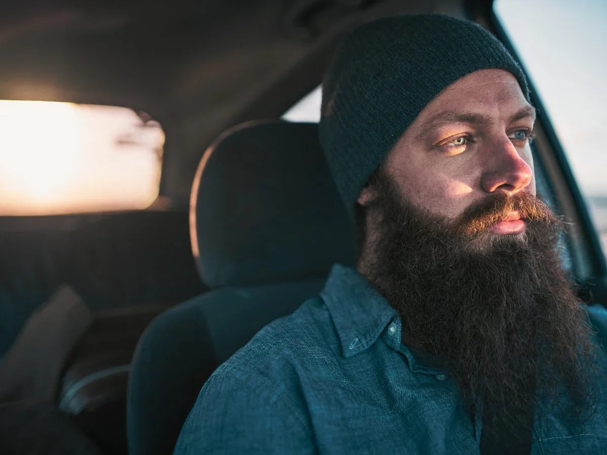 Man with thick beard and beanie hat sitting in car, natural winter light, beard care style