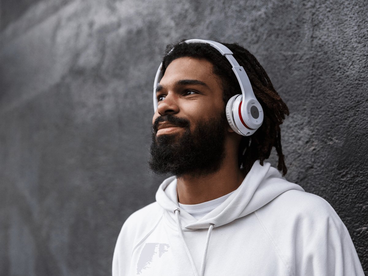 Man with thick beard and headphones wearing white hoodie against textured wall