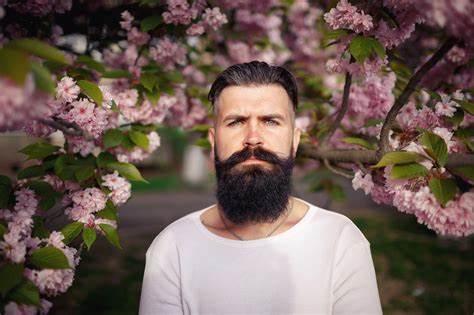 Bearded man with groomed dark beard and mustache standing outdoors among blooming spring flowers