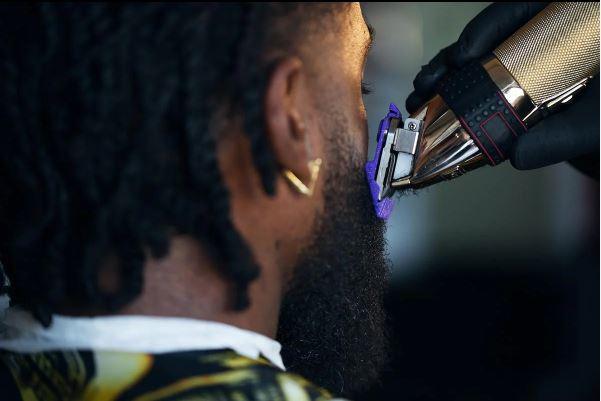 Barber trimming a man's beard with electric clippers, beard care routine closeup