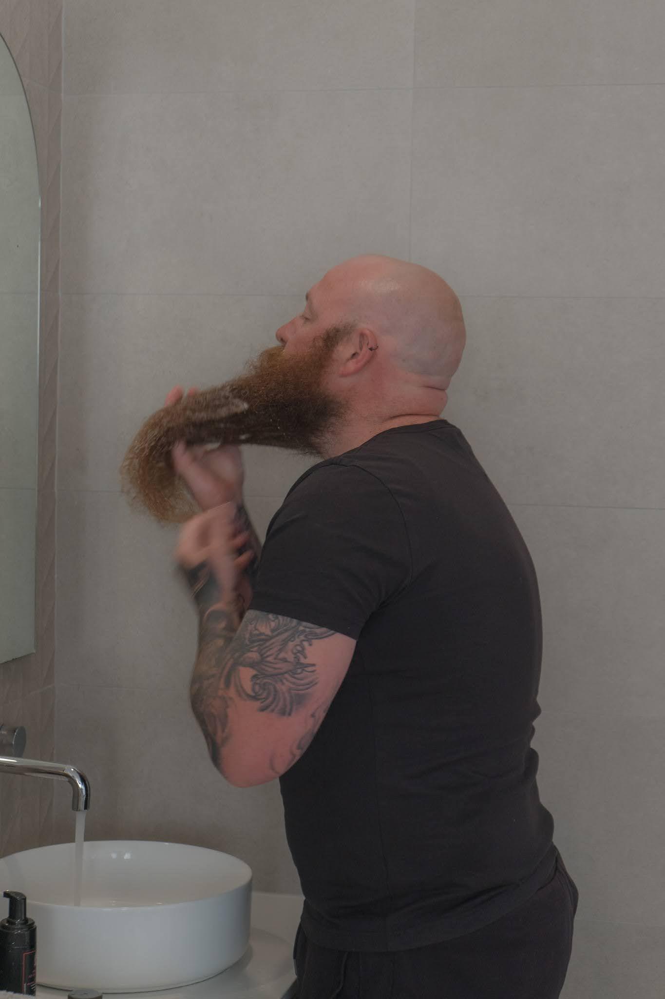 Man applying beard oil in bathroom, grooming long beard, self-care routine