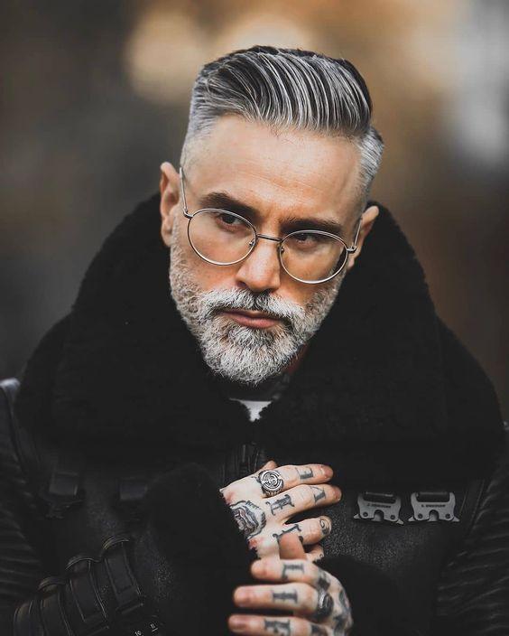 Stylish man with a gray beard, glasses, and tattoos in a warm winter jacket outdoors