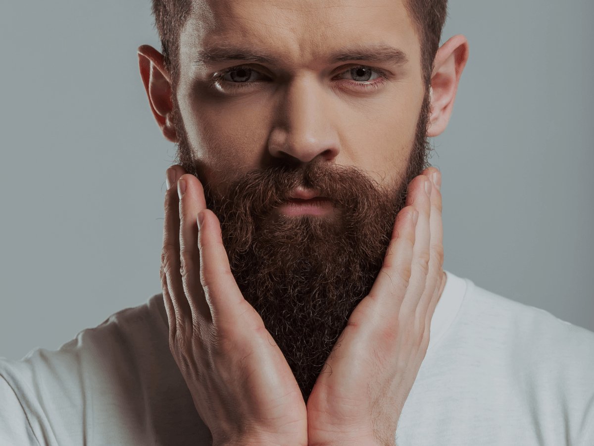 Man with full thick beard touching his face, showcases healthy beard growth care