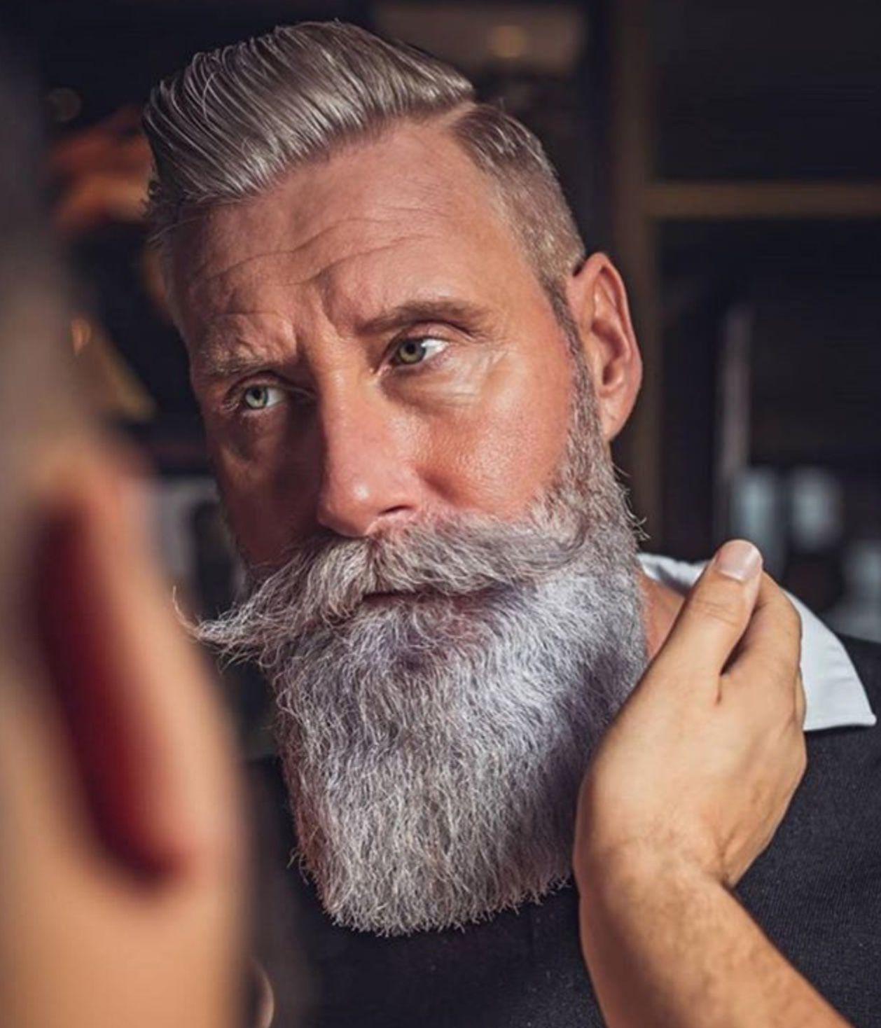 Man with a thick, styled grey beard and mustache receiving beard grooming care