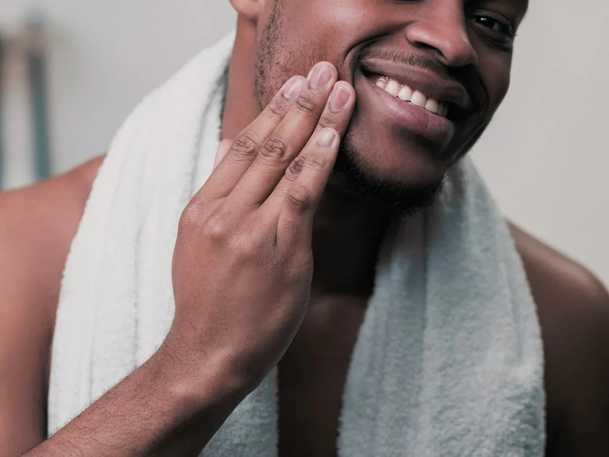 Smiling man with towel applies beard butter for grooming and hydration
