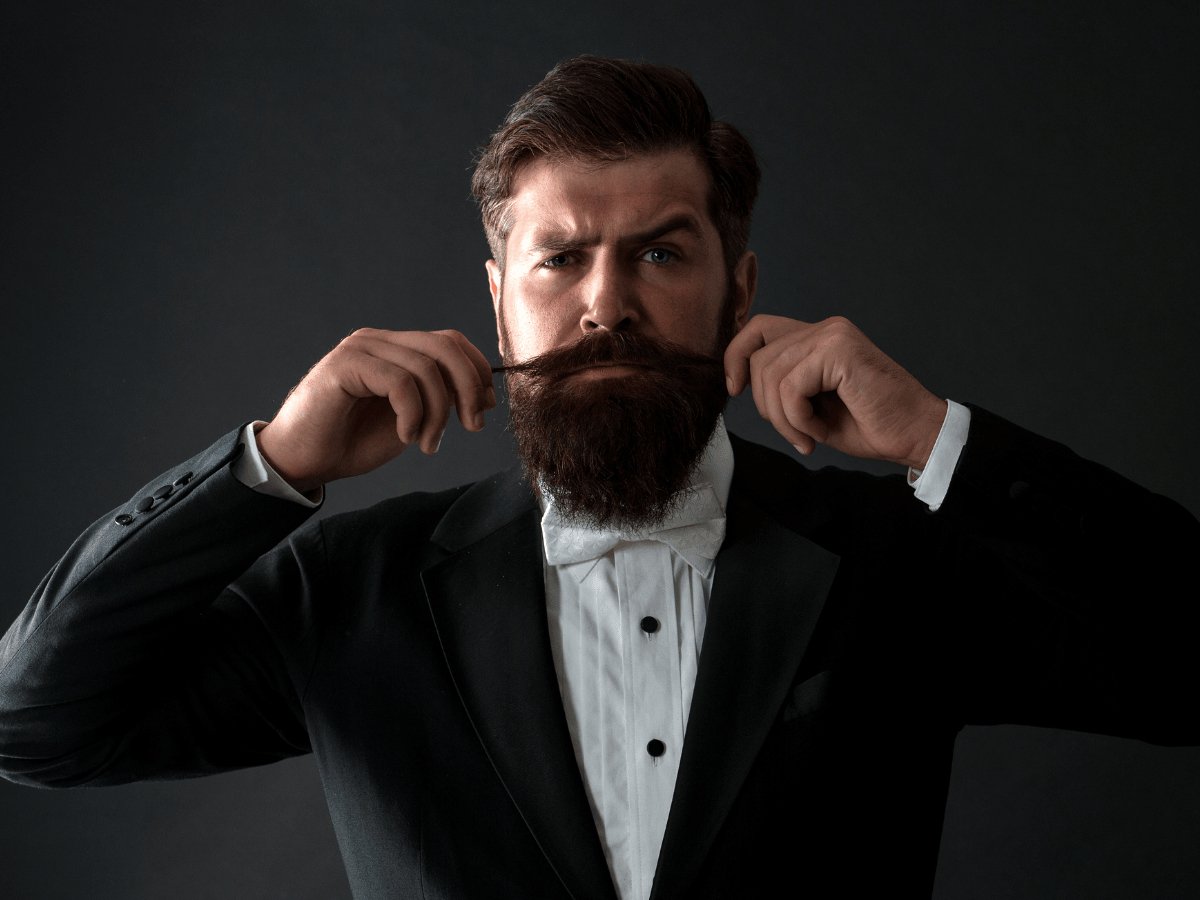 Man in tuxedo styling thick beard and moustache, grooming product concept