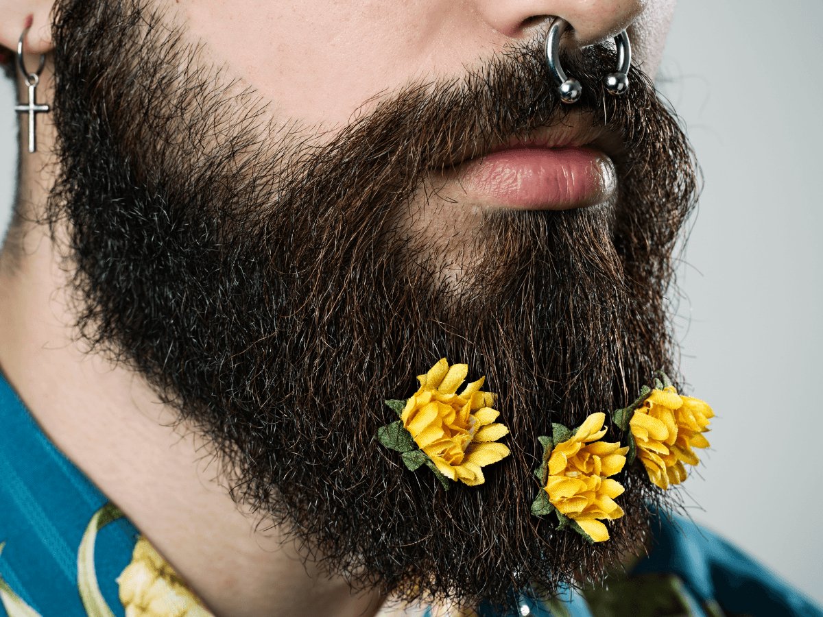 Close-up of a thick beard with yellow flowers, nose piercing, and cross earring, spring beard care