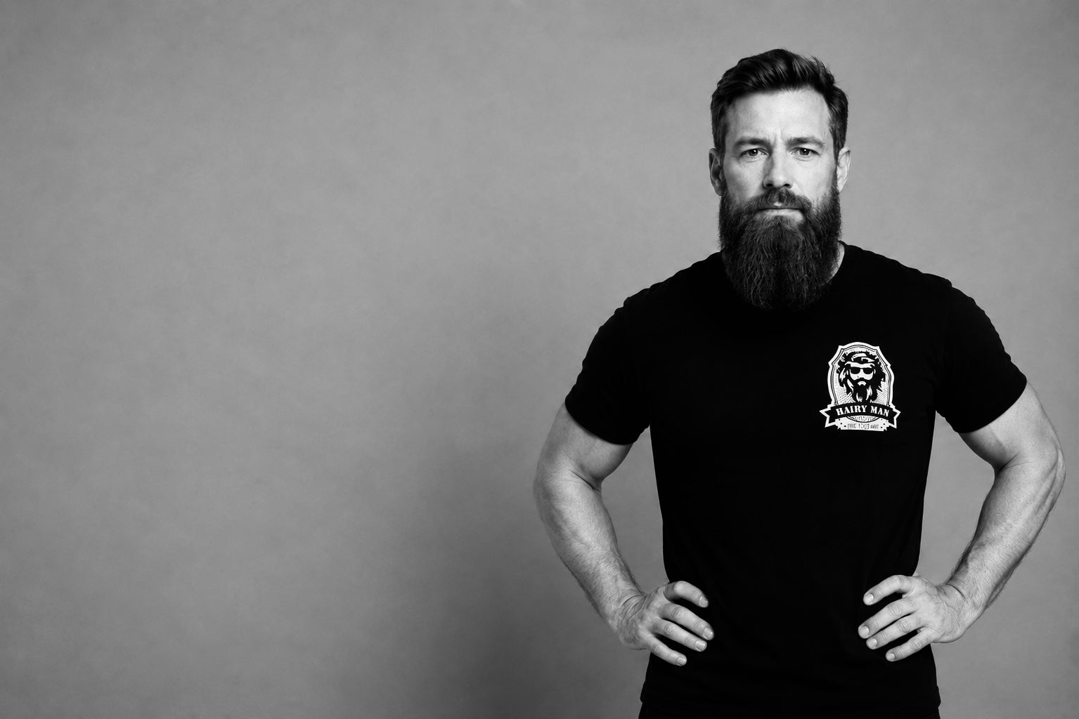 Close-up of bearded man wearing Hairy Man Care logo t-shirt, black background, natural beard.