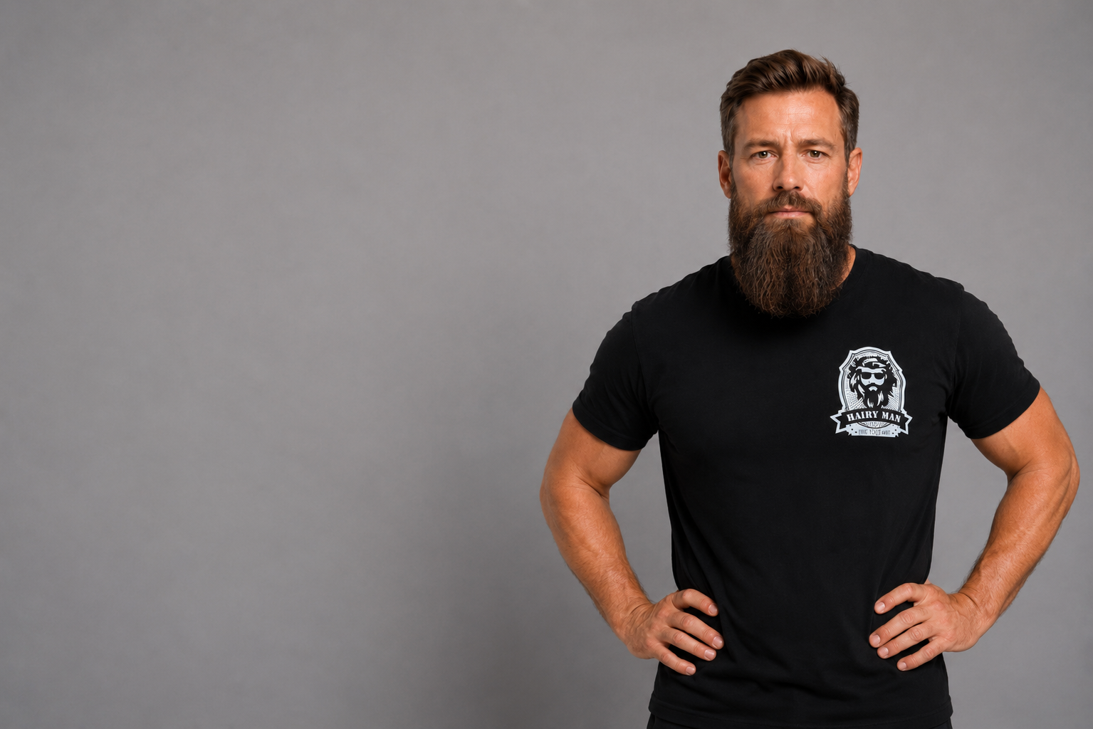 Close-up of bearded man wearing Hairy Man Care logo t-shirt, black background, natural beard.