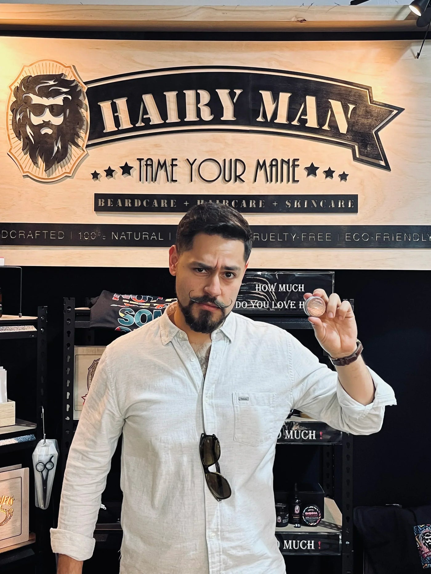 Bearded man holding beard balm tin at Hairy Man Care booth, beard care product display