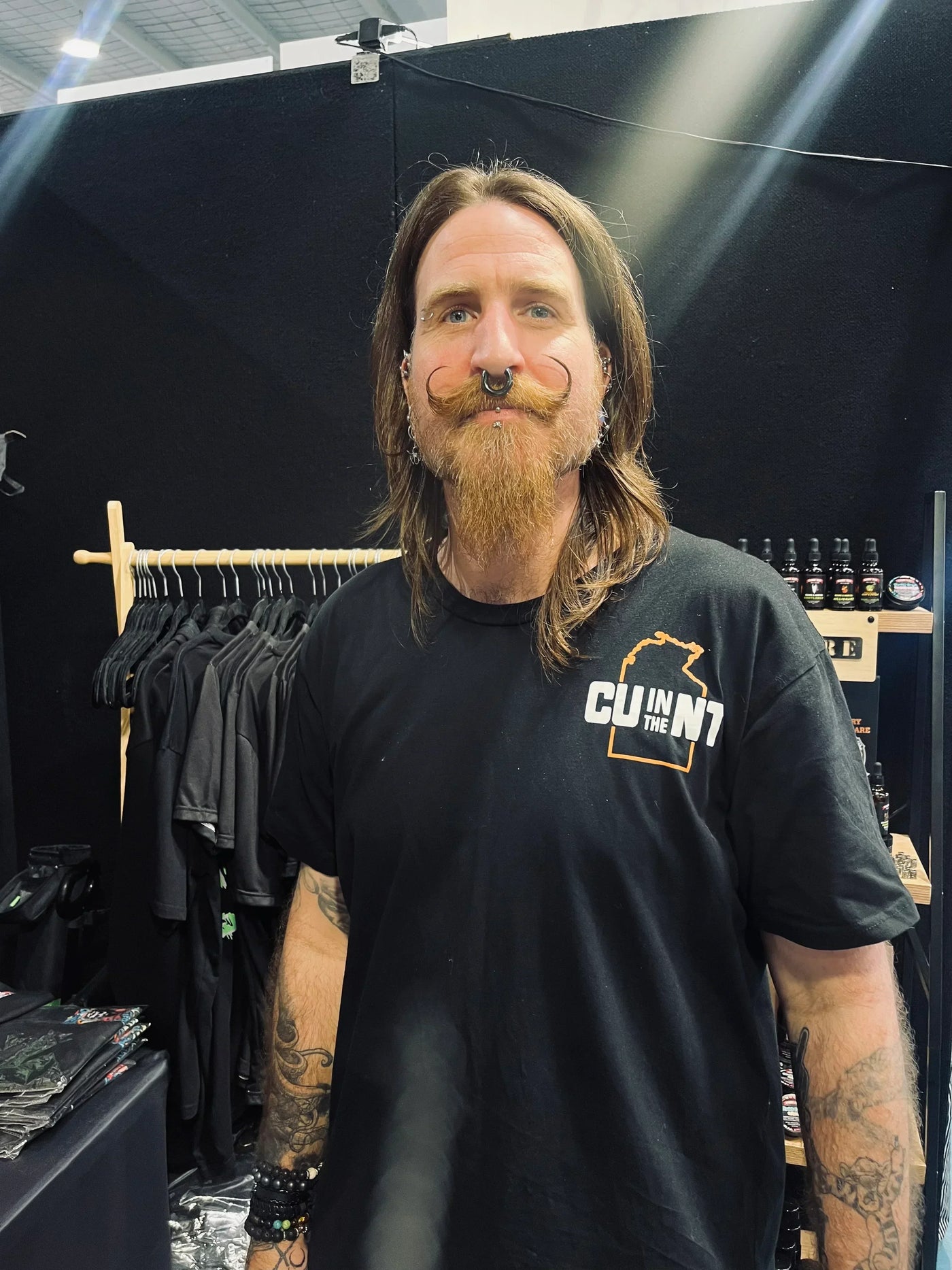 Bearded man with styled mustache and tattoos at Hairy Man Care display with beard care products