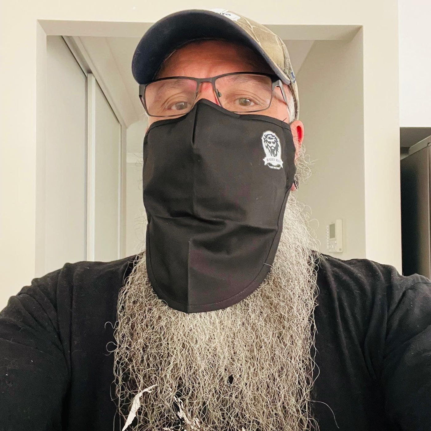 Man with long grey beard wearing black beard-friendly face mask and cap, showcasing beard care product fit