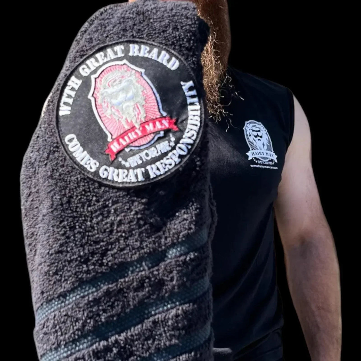 Bearded man holding black towel with 'With Great Beard Comes Great Responsibility' patch, wearing Hairy Man tank top