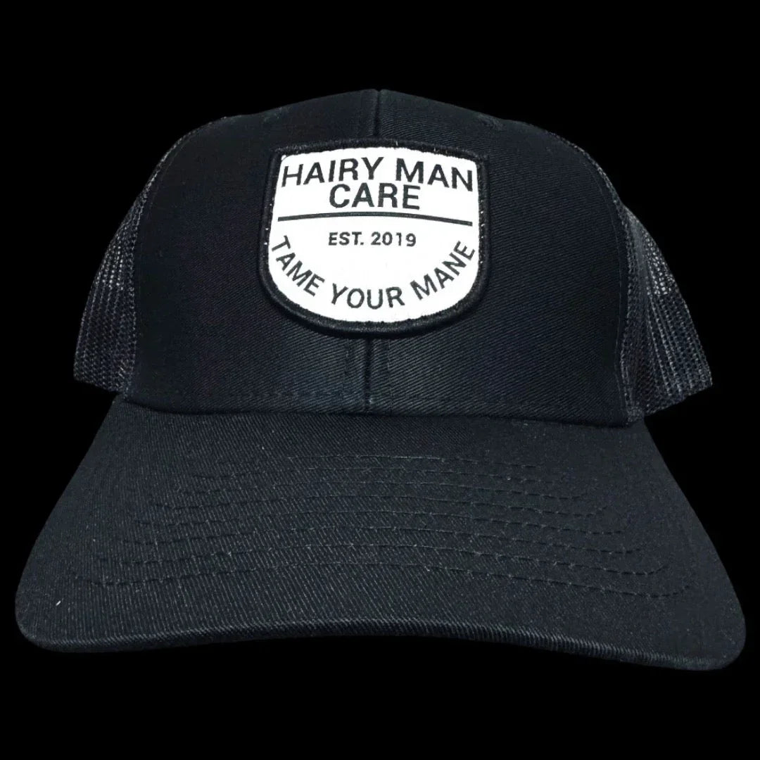 Black trucker hat with 'Hairy Man Care' logo, 'Tame Your Mane' slogan, est. 2019 patch