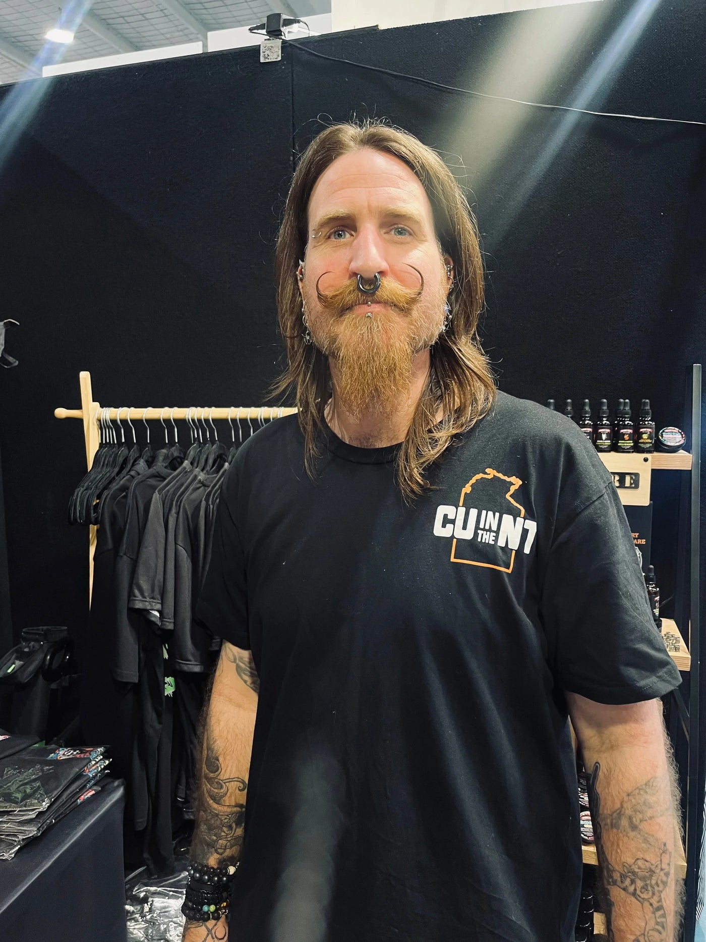 Man with long hair, beard, and mustache at beard care booth, showcasing natural grooming products